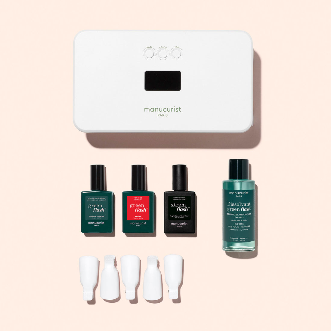 The Manucurist Discovery Kit features a white LED lamp, three nail polishes, a vitaminized base coat, remover, and four white nail clips—perfect for an ultra-glossy manicure—beautifully displayed on a light pink background.