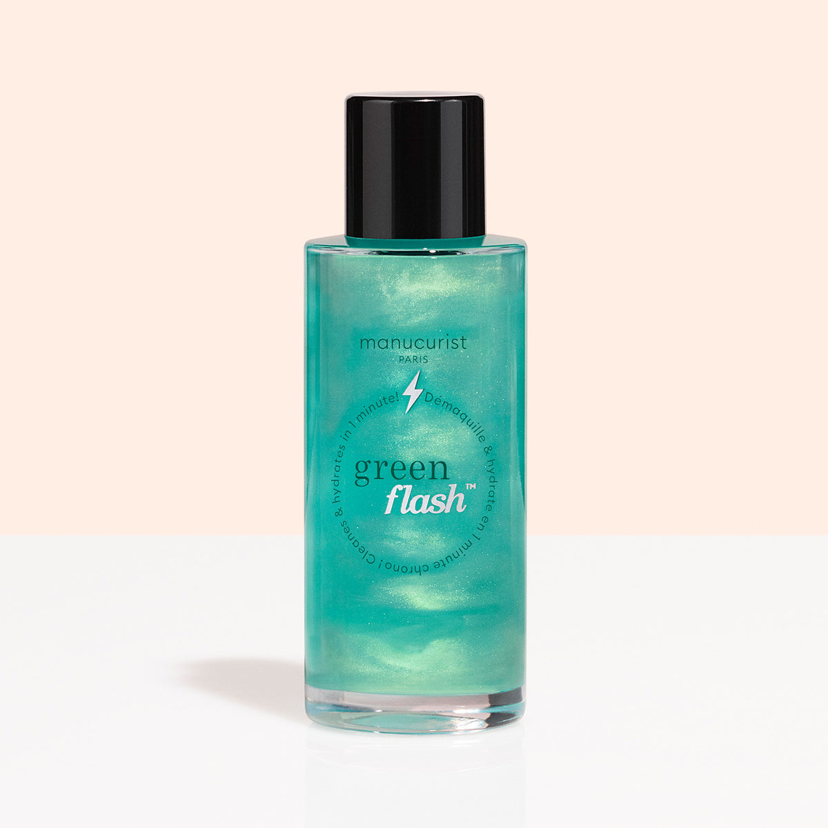 A clear bottle with a black cap, labeled “Manucurist Green Flash™ Gentle Glitter Remover,” holds shimmery teal, acetone-free liquid and is displayed against a light peach and white background.