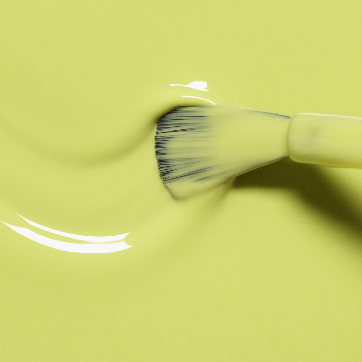 Gros plan sur un pinceau appliquant la teinte Lime de Manucurist, un vert anis lisse et brillant, sur une surface jaune. Des courbes fluides et une texture subtile mettent en valeur l&