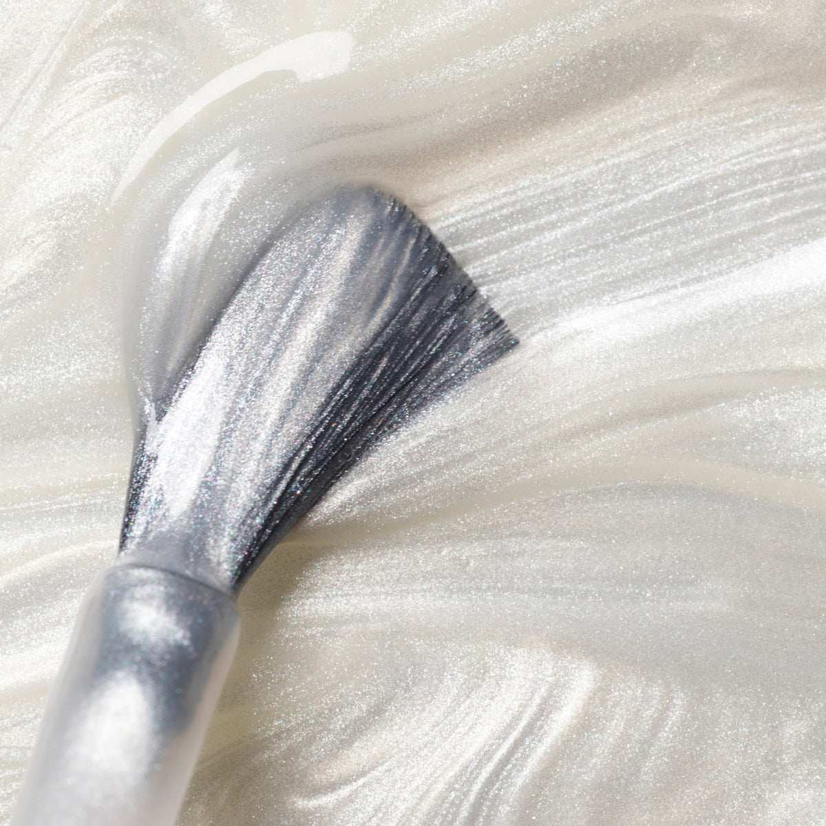 Gros plan d’un pinceau appliquant le vernis à ongles blanc nacré scintillant Moon de Manucurist, créant des stries lisses et brillantes sur une surface.