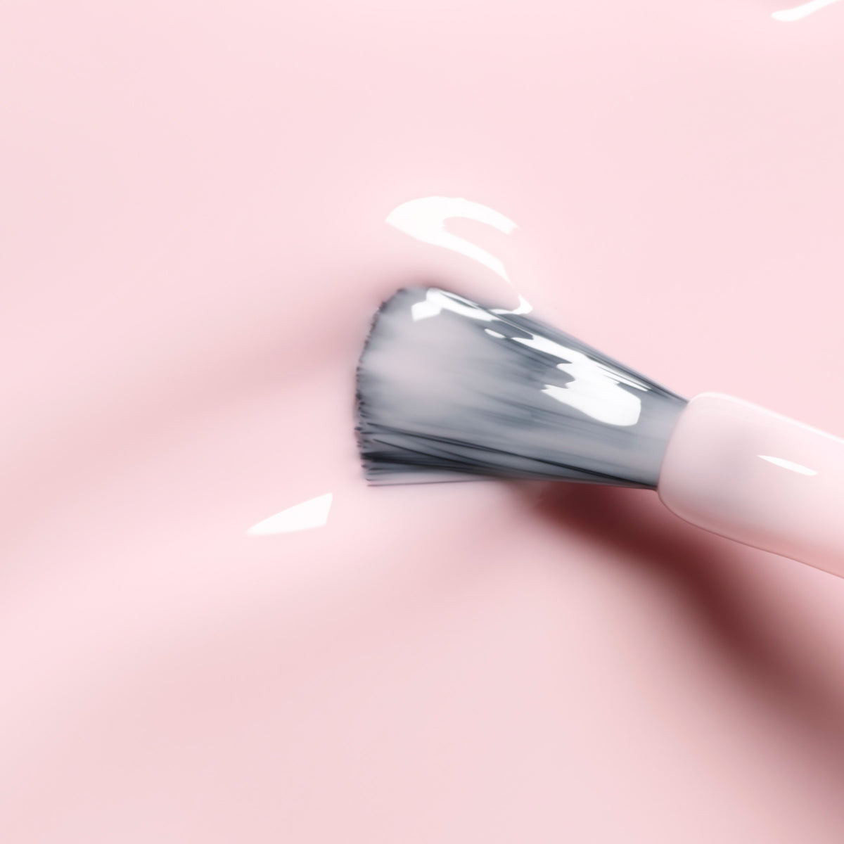 Gros plan d’un pinceau de maquillage appliquant le vernis à ongles Milky Pink de Manucurist, créant un fini crémeux et brillant sur une surface lisse rose clair.