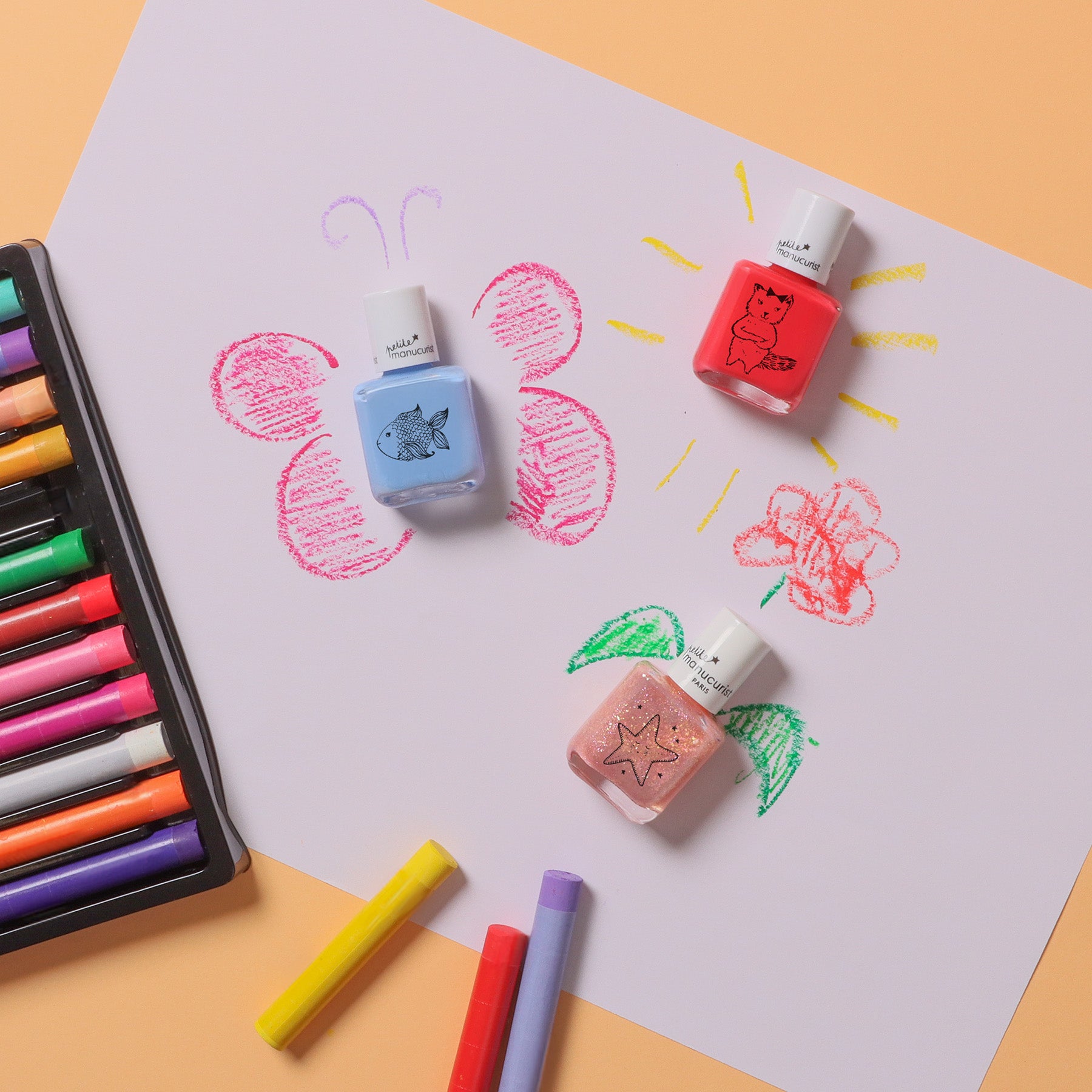 Three nail polish bottles with doodles on them are placed on a colorful childs drawing featuring a butterfly, flower, and sun, with a set of colored markers and marker caps beside the paper on a peach background.