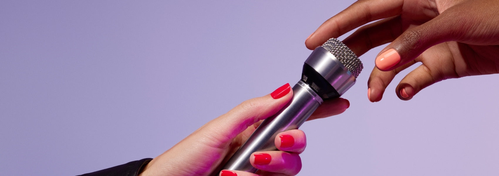 Two hands with brightly painted nails exchange a silver microphone against a purple background.