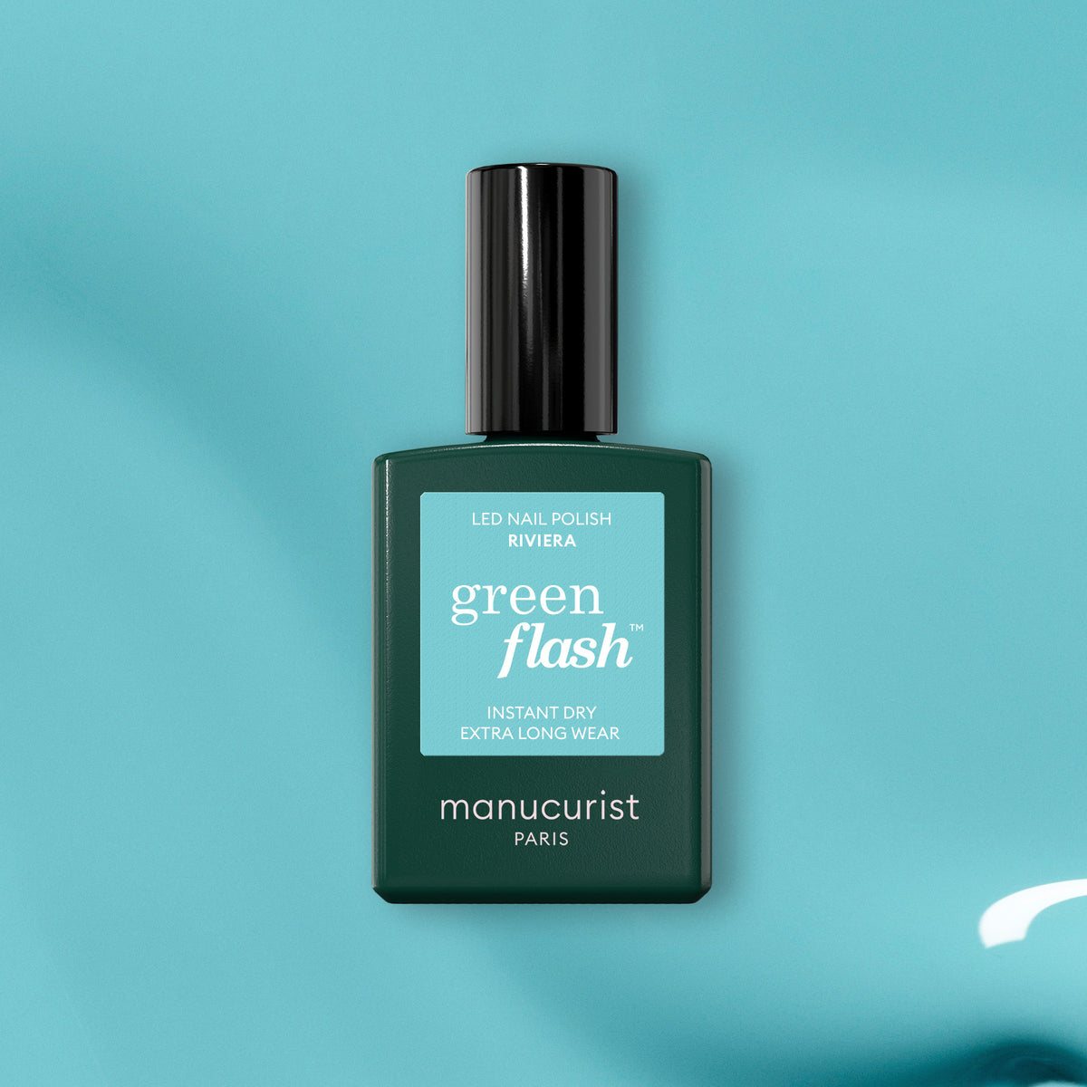 Un flacon vert de vernis gel Riviera de Manucurist repose sur une surface bleu sarcelle, mettant en avant ses propriétés de séchage instantané et de tenue extra longue.