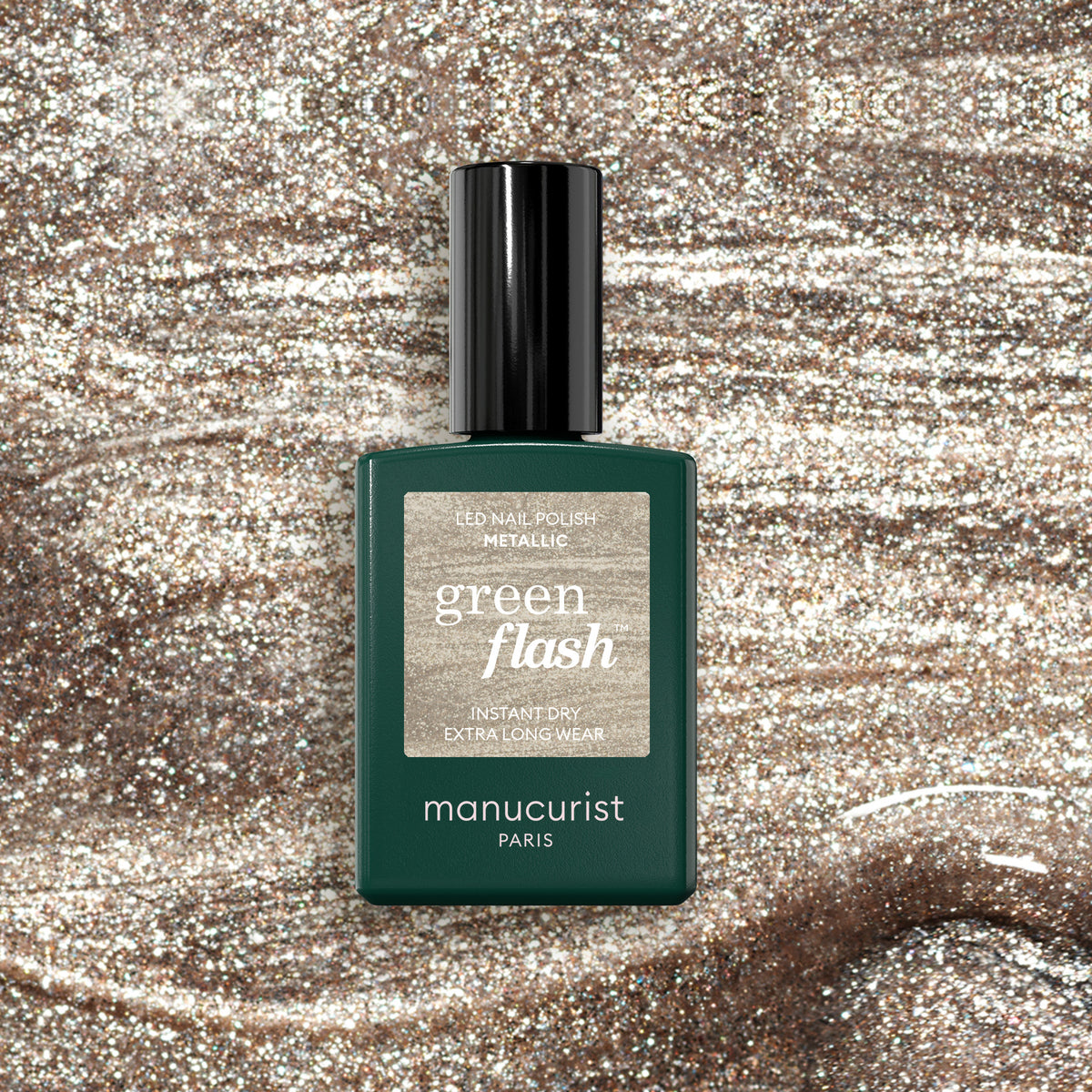 Un flacon de vernis à ongles Métallique Manucurist posé sur une surface scintillante qui reflète le shimmer doré aux tons froids et les reflets métalliques du vernis.