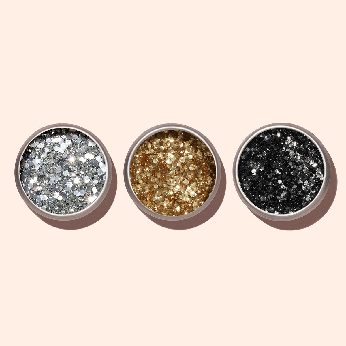 Trois petits pots ronds de paillettes biodégradables argentées Manucurist sont disposés en rangée sur un fond beige clair — idéal pour un vernis à ongles éco-responsable ou un nail art argenté éclatant.