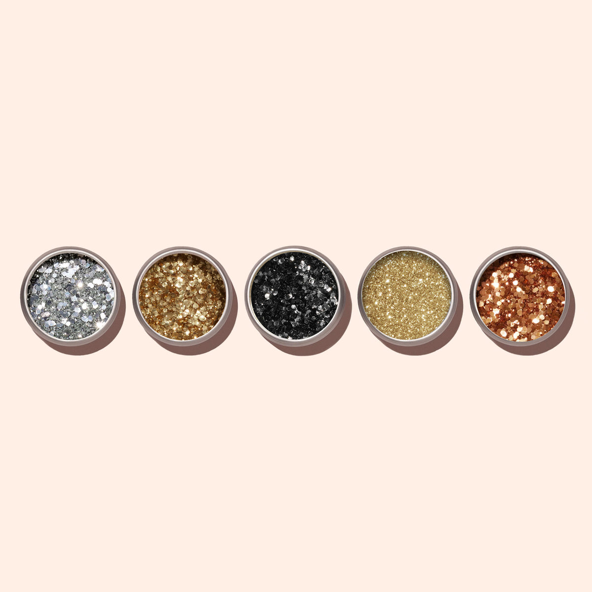 Five small round containers of Manucurist Golden Chrome Powder in silver, gold, black, light gold, and copper are arranged in a row on a beige background—ideal for a chrome finish or layering over gel polish.