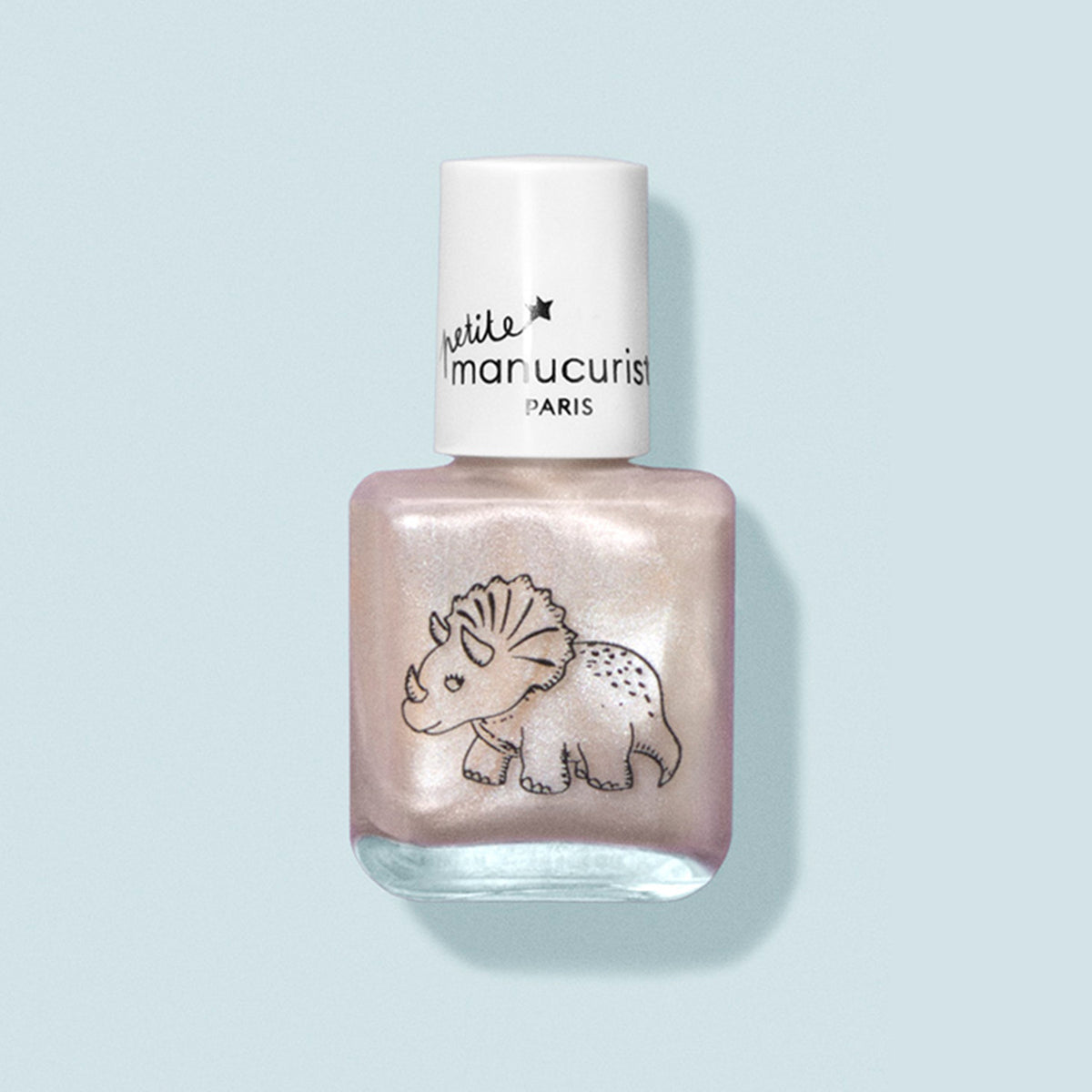 A bottle of water-based, pearlescent pink kids nail polish called “Pénélope the Triceratops” by Manucurist, with a white cap and cute triceratops design on the front, shown against a light blue background.