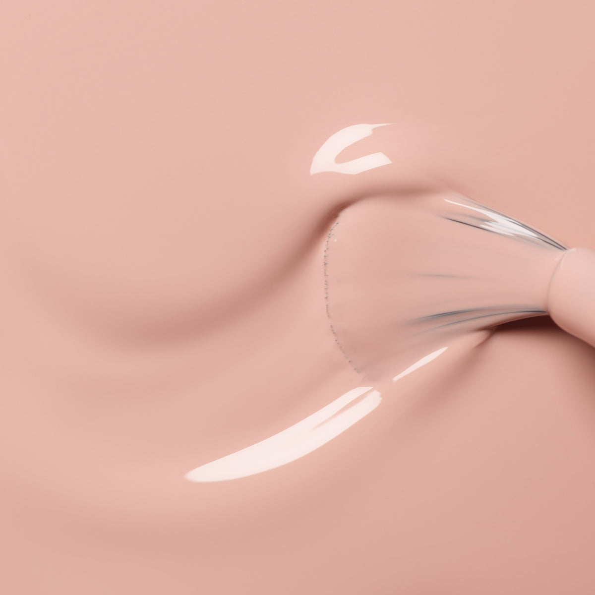 Gros plan sur un pinceau à ongles appliquant un vernis à ongles rose nude brillant, créant des touches lisses et un fini brillant sur une surface rose clair.