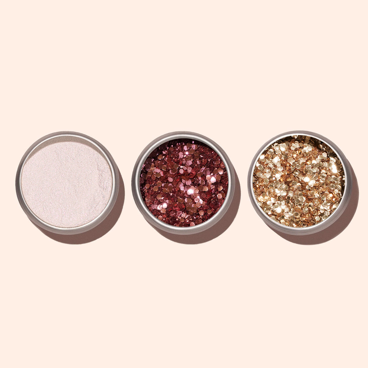 Three open small round containers hold loose powders—white shimmer, Manucurist Rose Gold Biodegradable Glitter, and gold glitter for nail art—arranged side by side on a light beige background.