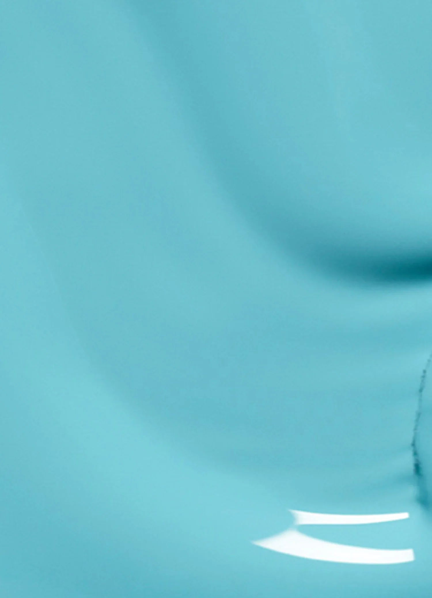 A close-up image of a smooth, light blue surface with gentle curves and subtle shading, featuring a shiny reflection and a faint crack or line near the bottom right.