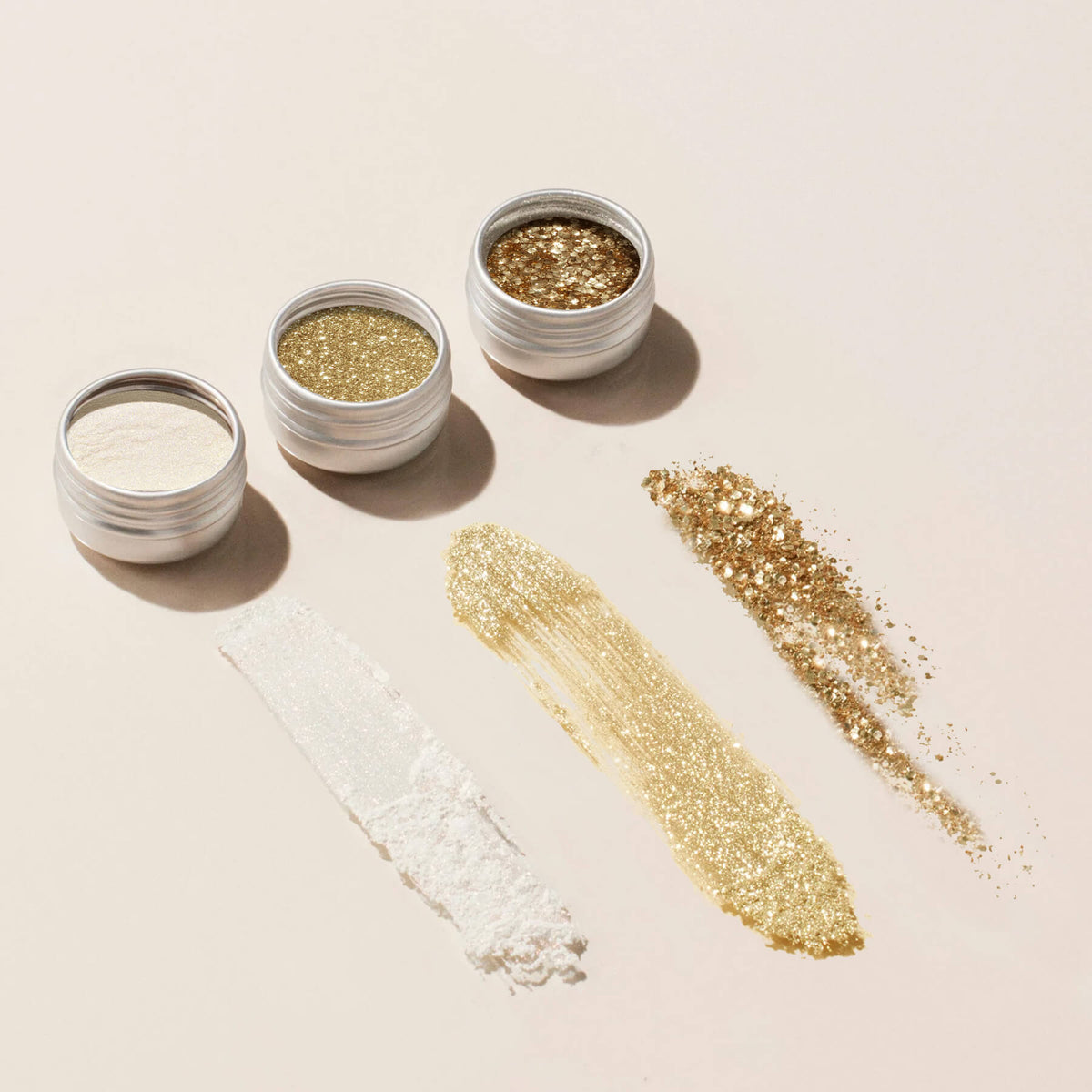 Trios de paillettes et poudres à effets Manucurist : trois petites boîtes de poudres scintillantes blanches, dorées et bronze sur un fond beige, idéales pour ajouter de l’éclat aux créations de vernis à ongles ou de gel.
