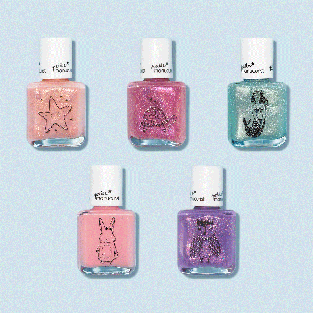 Five Customizable 5-pack Petite Manucurist nail polishes by Manucurist rest on a light blue background, each with playful black outline designs—starfish, turtle, mermaid, rabbit, and owl—a whimsical rainbow set for kids.