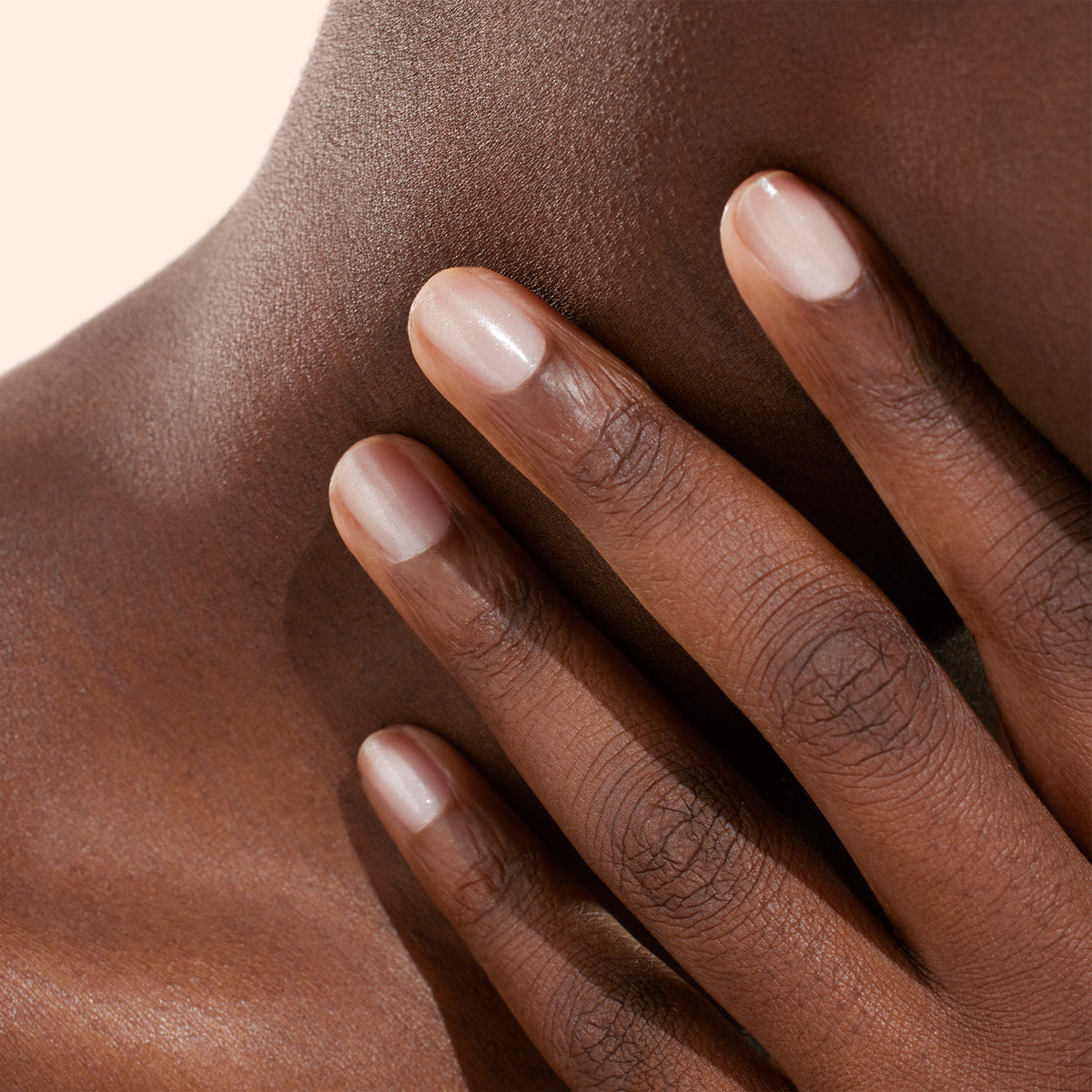 Gros plan d’une main aux ongles soigneusement manucurés, vernis avec le vernis à ongles biosourcé Active™ Shine Opal de Manucurist, touchant délicatement le côté du cou et la clavicule d’une personne sur un fond neutre.