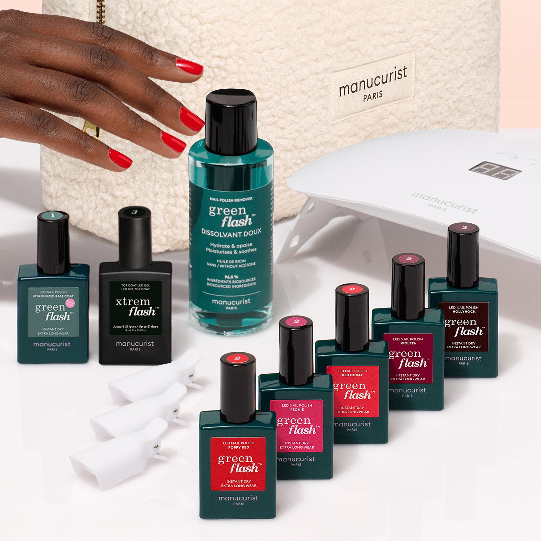 A hand with red nails reaches for the Manucurist Super Starter Kit, which includes remover, vitaminized base coat, top coat, nail clips, a manicure lamp, and a cream Manucurist Paris bag—everything needed for an ultra-glossy manicure.