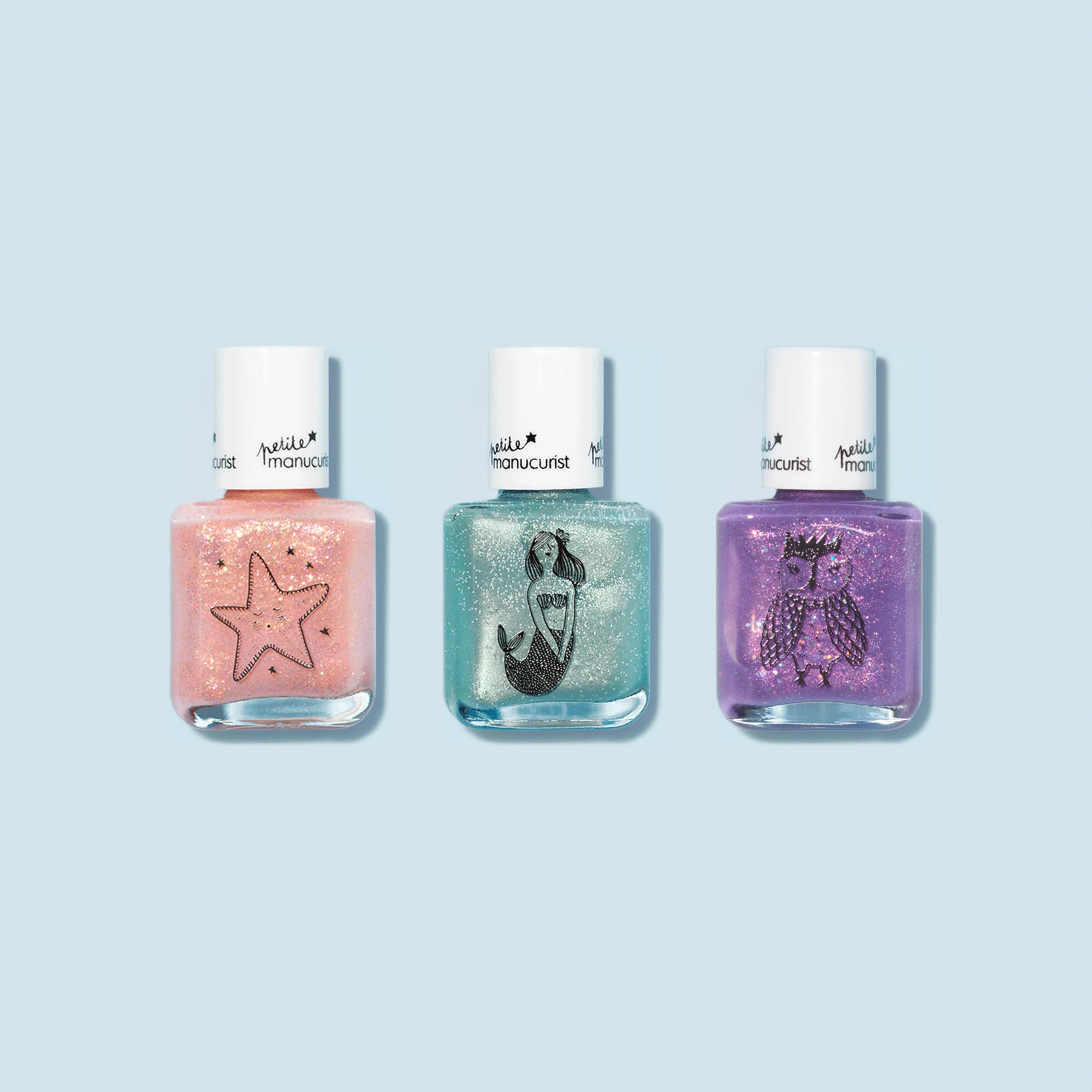 The Manucurist Customizable 3-pack Petite Manucurist set features kids nail polishes in sparkly peach, teal, and purple, each with a white cap and cute black starfish, mermaid, and owl illustrations on the front.