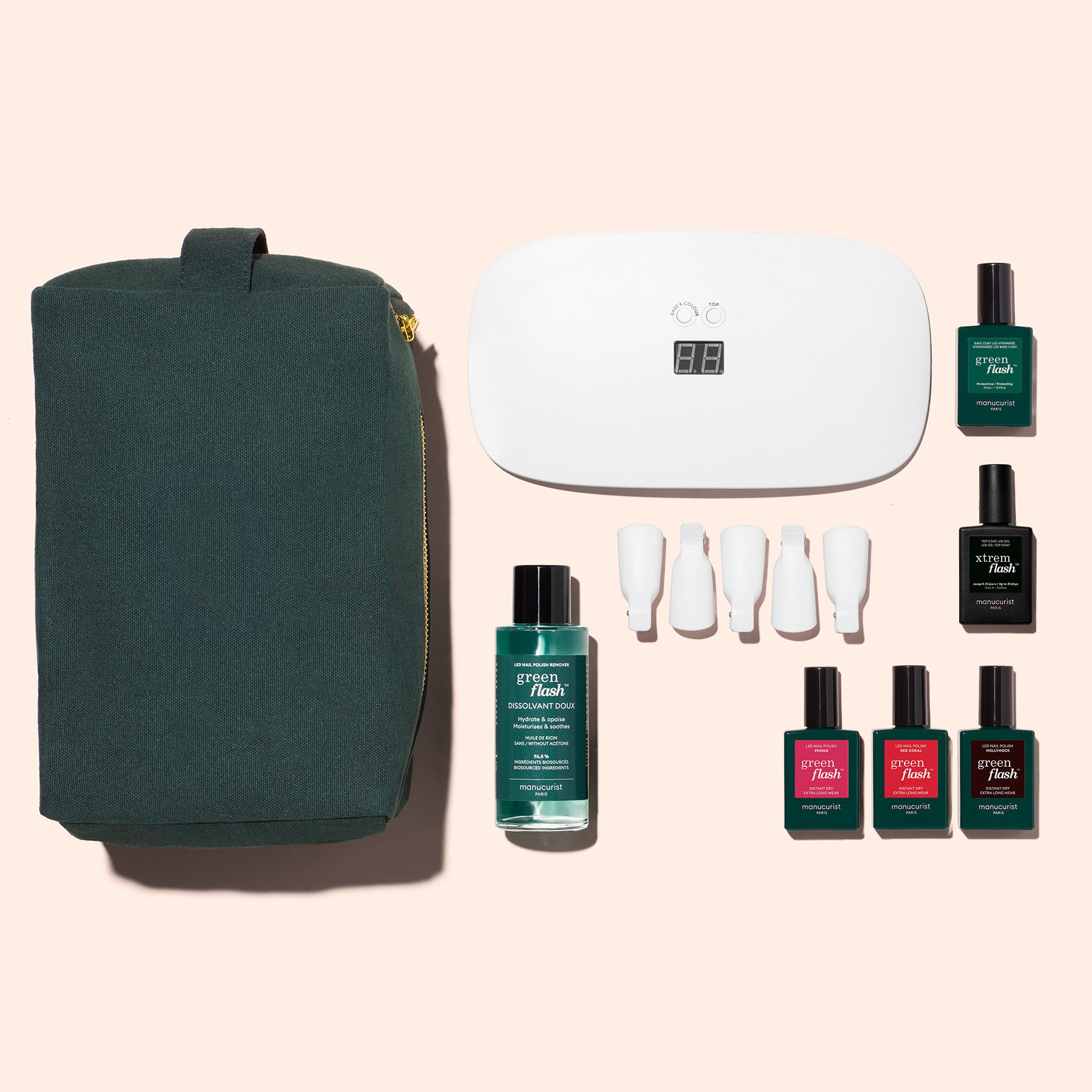 The Manucurist Super Starter Kit features a dark green pouch, white UV nail lamp, four nail tools, remover, and six green and red gel polishes—perfect for an ultra-glossy manicure on a light beige background.