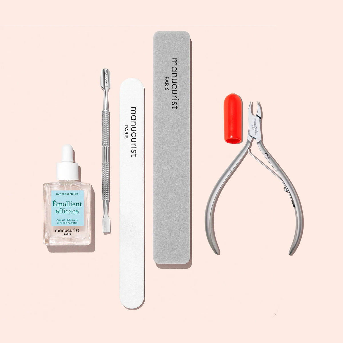 Le Kit Préparation Ongles Manucurist comprend une huile émolliente pour cuticules, un repousse-cuticules en métal, une lime à ongles émeri, un polissoir et une pince à cuticules en acier inoxydable avec capuchon rouge, présentés sur fond rose clair.