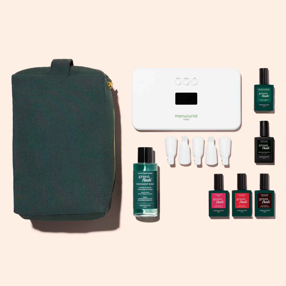 The Manucurist Starter Kit includes a dark green zippered pouch, white manicure lamp, remover, four white nail caps, and six bottles—one is a vitaminized base coat—for an ultra-glossy manicure on a pale pink background.