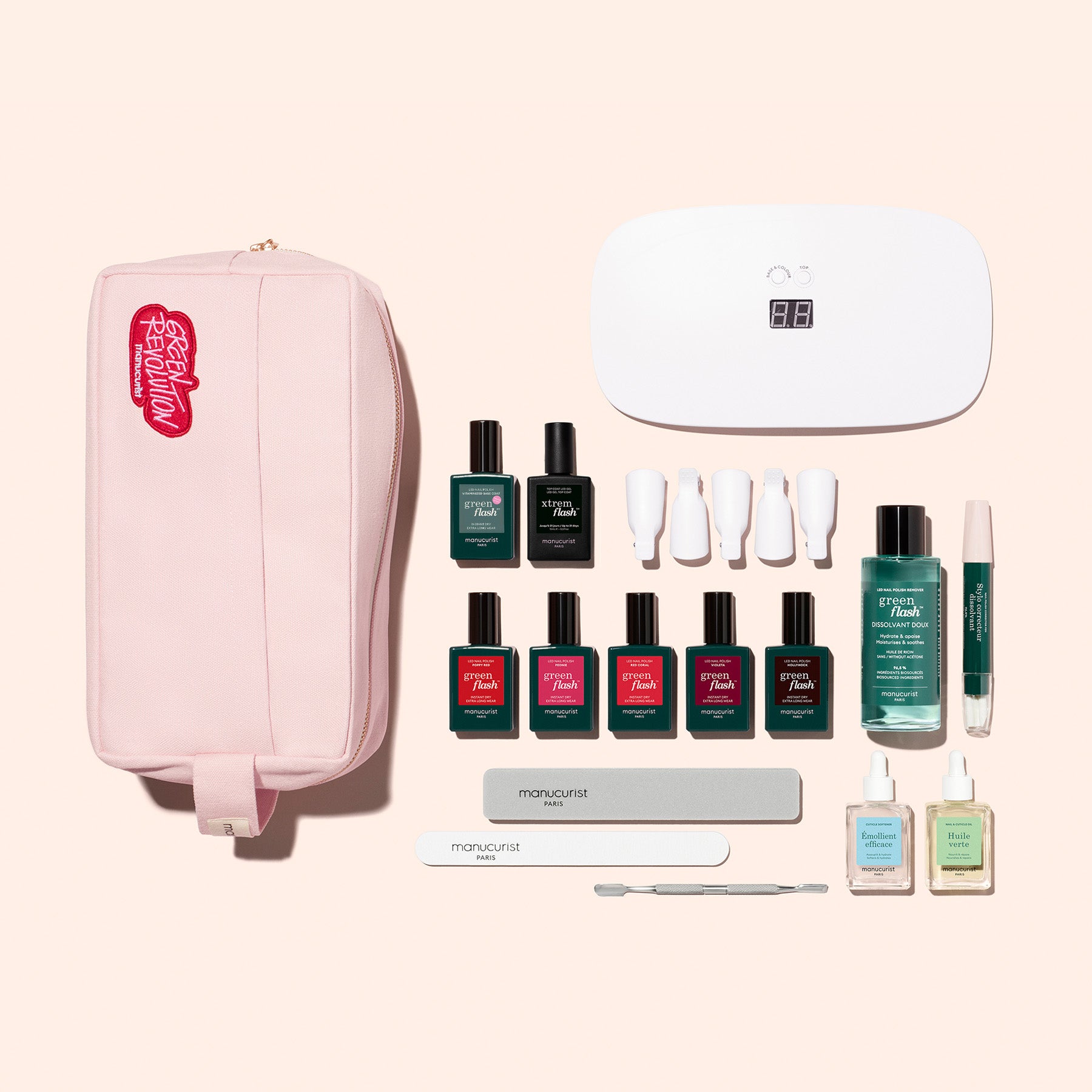 The Manucurist Super Ultimate Kit includes a pink bag, white LED nail lamp, multiple Green Flash gel polishes, nail files, cuticle tools, vitaminized base coat, and nail care liquids displayed on a beige background.
