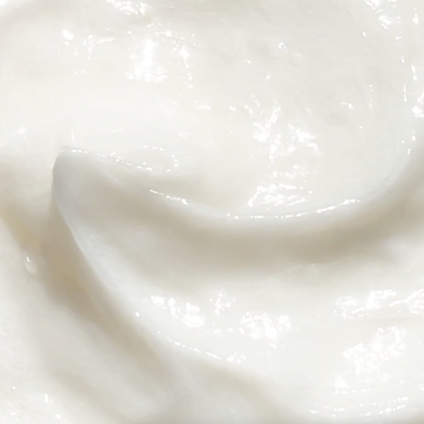 Close-up of a smooth, creamy white substance with a glossy texture, possibly yogurt, sour cream, or lotion, showing gentle swirls and soft peaks.