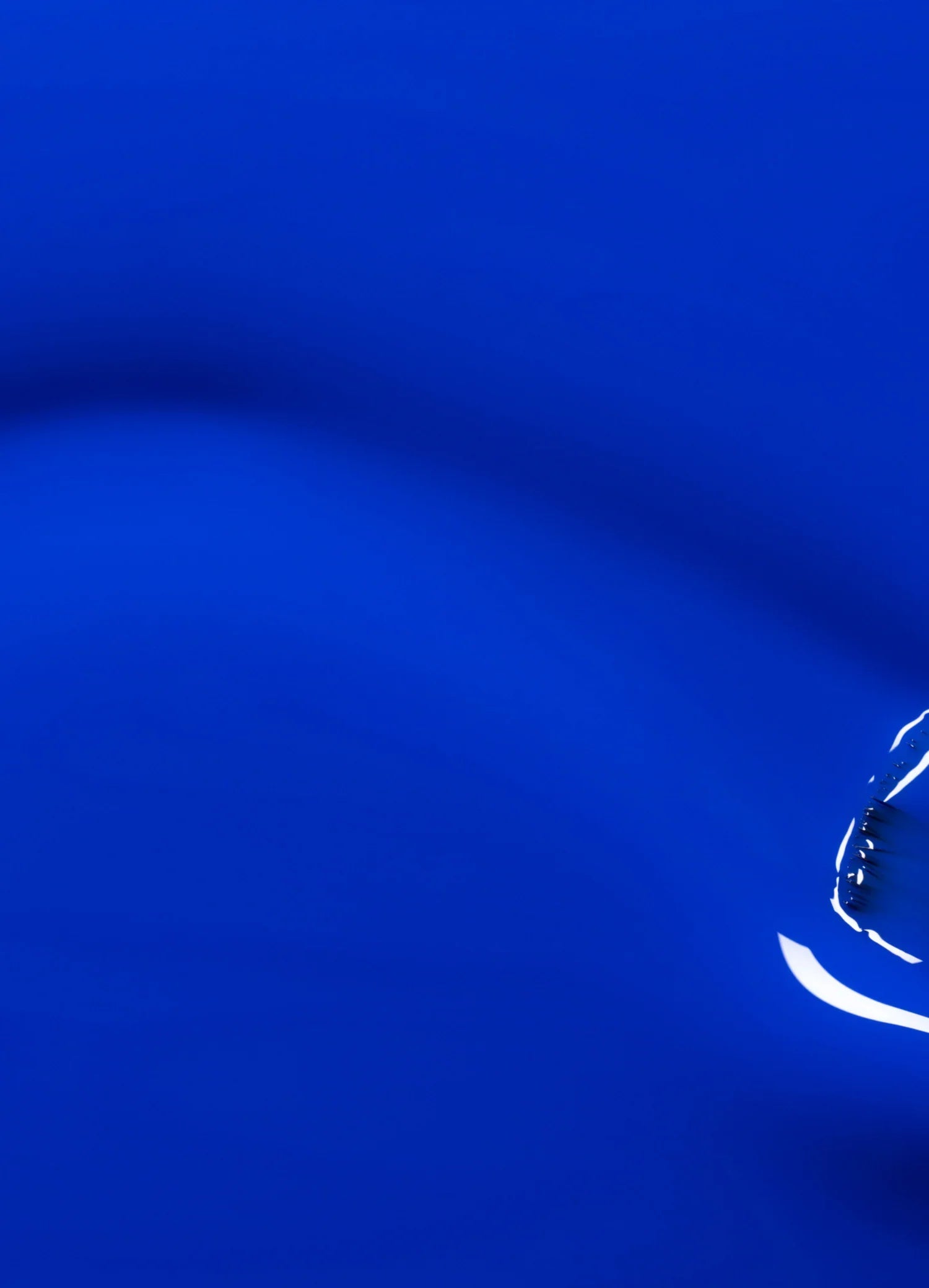 A single water droplet creates ripples on a smooth, vivid blue surface, with light reflections enhancing the sense of motion and fluidity.
