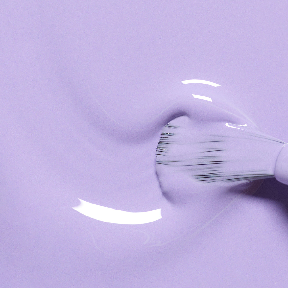 Gros plan sur le pinceau Manucurist Wisteria glissant sur une surface lisse, déposant un vernis violet pastel aux sous-tons bleu froid en créant de douces ondulations et des reflets lumineux.