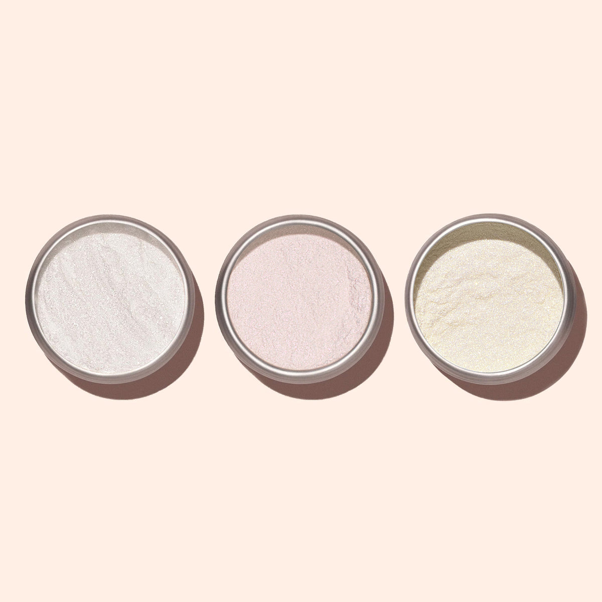Trois petits pots ronds de Poudre Effet Glacé Rose Manucurist, dans les teintes blanc, rose clair et jaune clair, sont disposés sur un fond pâle, chacun apportant un éclat délicatement nacré pour un fini subtilement glazed.