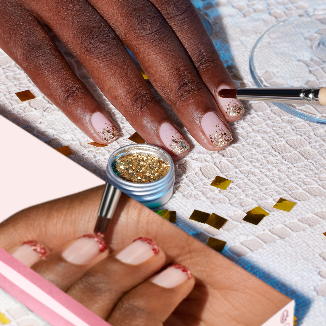 A hand with light pink nails is decorated using the Manucurist Glitter Brush with vegan synthetic bristles and gold glitter. The brush and glitter are shown close-up on a pink background sprinkled with gold confetti.