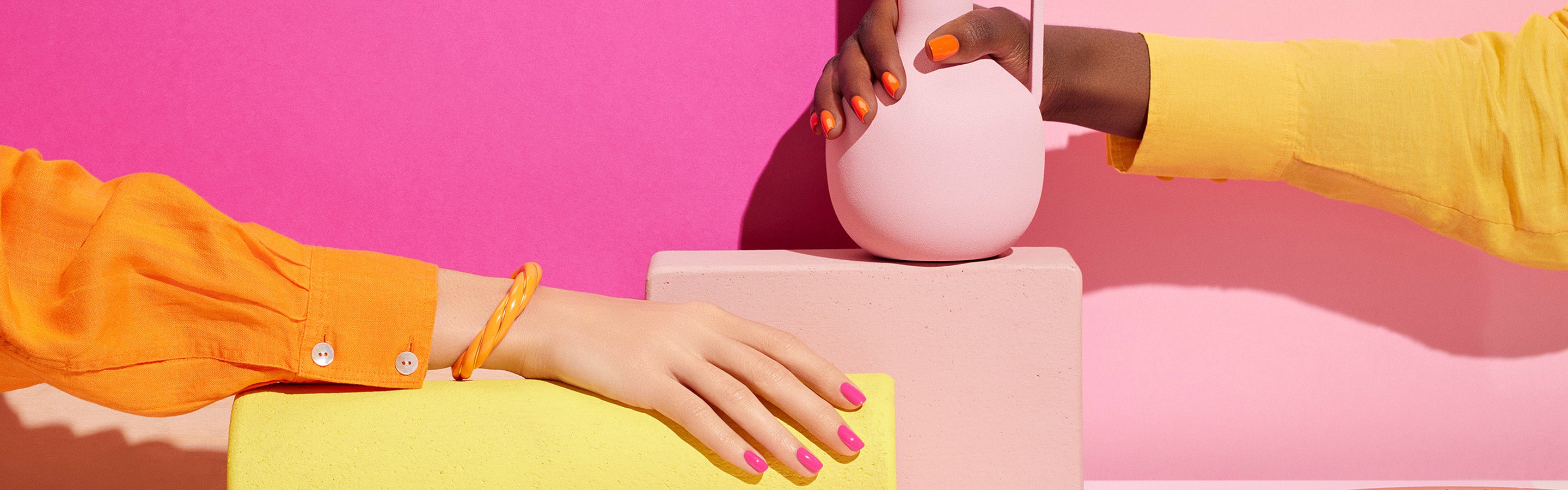 Two arms with brightly painted nails—one light-skinned, one dark-skinned—reach across colorful geometric blocks. Both wear yellow-orange shirts, and the background features bold pink, peach, and yellow shades.