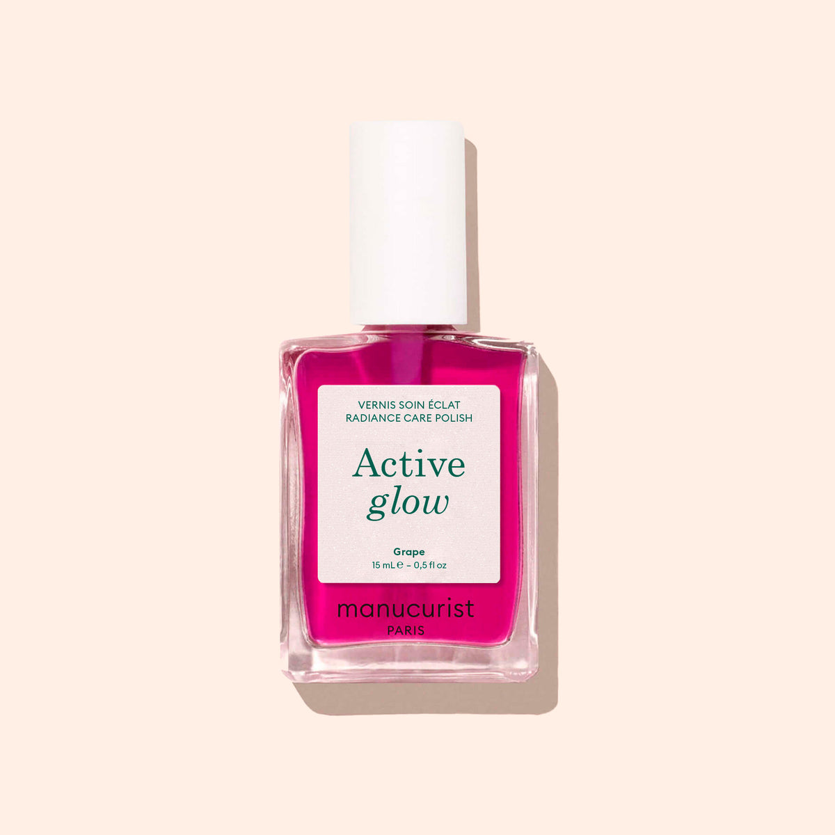 Un flacon de soin pour les ongles Active™ Glow Grape de Manucurist, avec un bouchon blanc et un liquide rose, conçu pour sublimer votre brillance naturelle, présenté sur un fond beige clair.