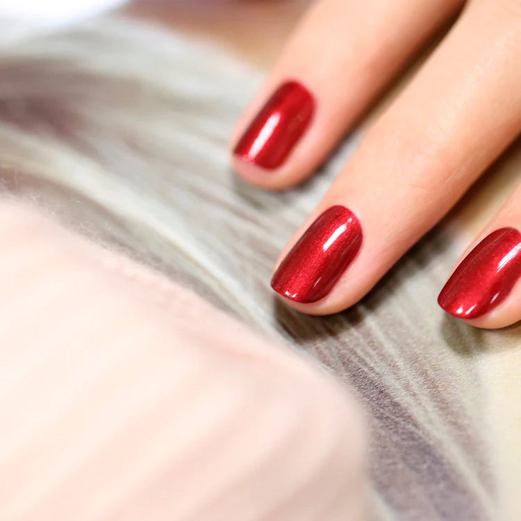 A close-up of a hand with glossy, red-painted fingernails resting on a soft, blurred surface.