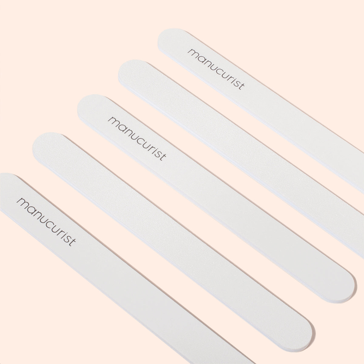 Cinq limes à ongles Manucurist sont disposées en diagonale sur un fond beige clair. Chaque lime, dotée d&