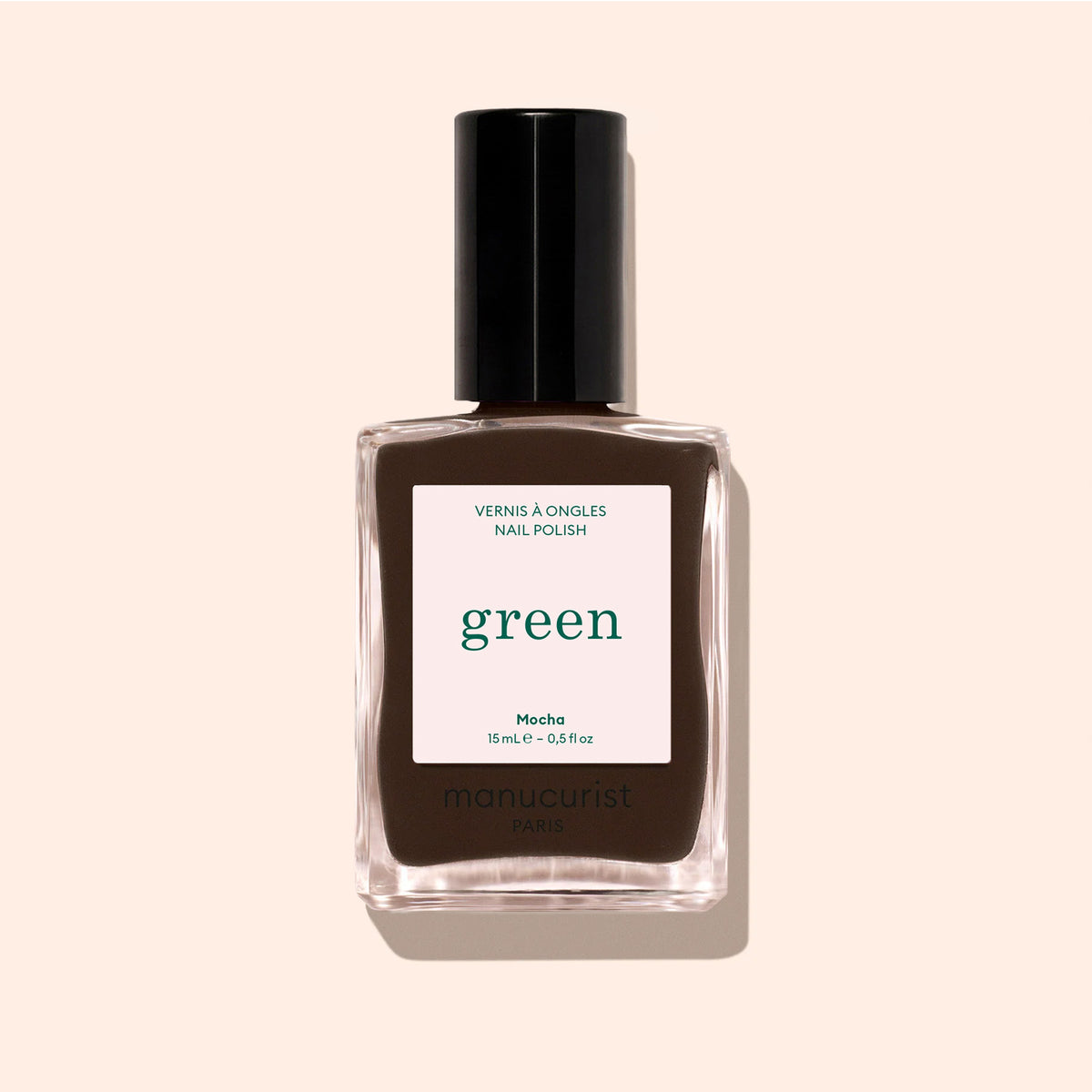 A bottle of Manucurist Mocha, a dark brown nail polish with cool undertones and a black cap labeled “green,” is shown against a pale beige background.