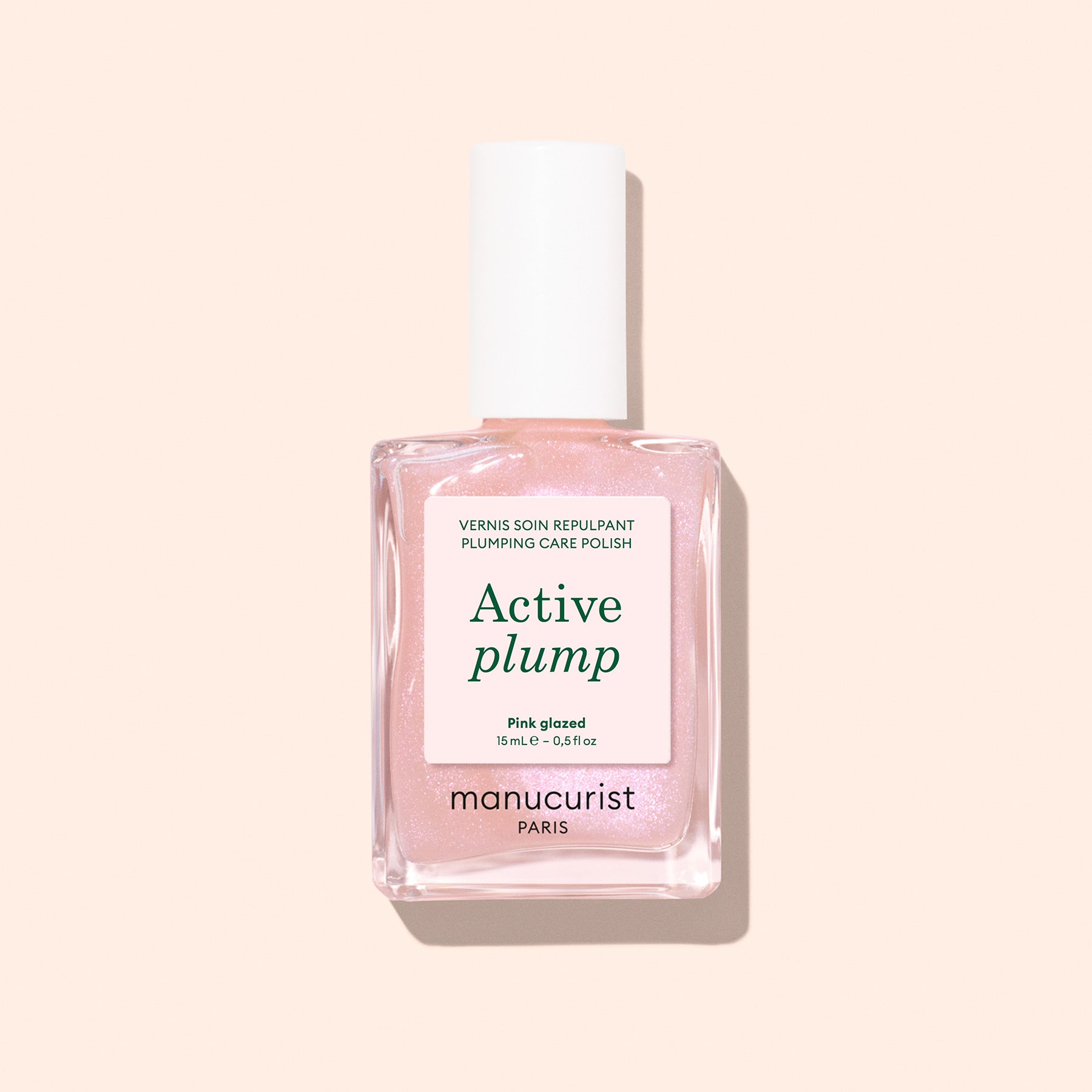 A bottle of Manucurist Active Plump Pink Glazed nail polish with a white cap and light pink liquid, set against a light beige background. The label mentions "Plumps hydrates for beautifully hydrated nails" and "Paris.