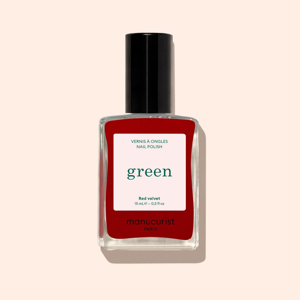 Un flacon de vernis à ongles Red Velvet de Manucurist de la gamme Green, avec un bouchon noir et une étiquette blanche "green", se détache sur un fond beige clair.