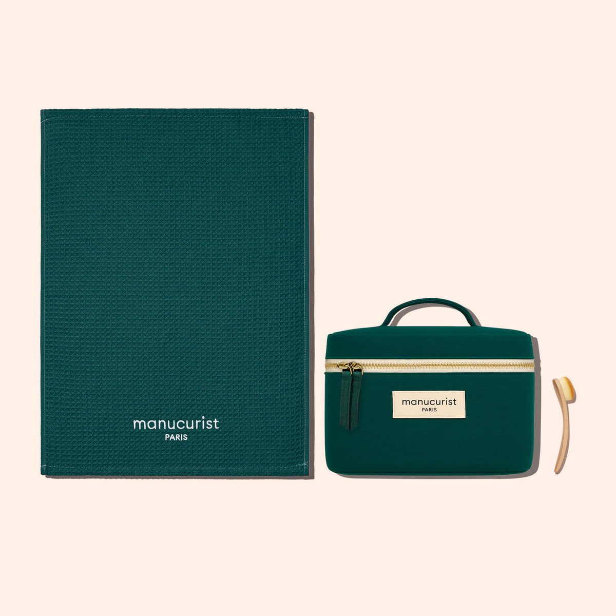 Une serviette en coton biologique texturé vert foncé Manucurist-us, une pochette zippée assortie avec anse et étiquette, et un petit bâtonnet repousse-cuticules en bois, le tout disposé sur un fond beige clair pour une protection douce des surfaces.