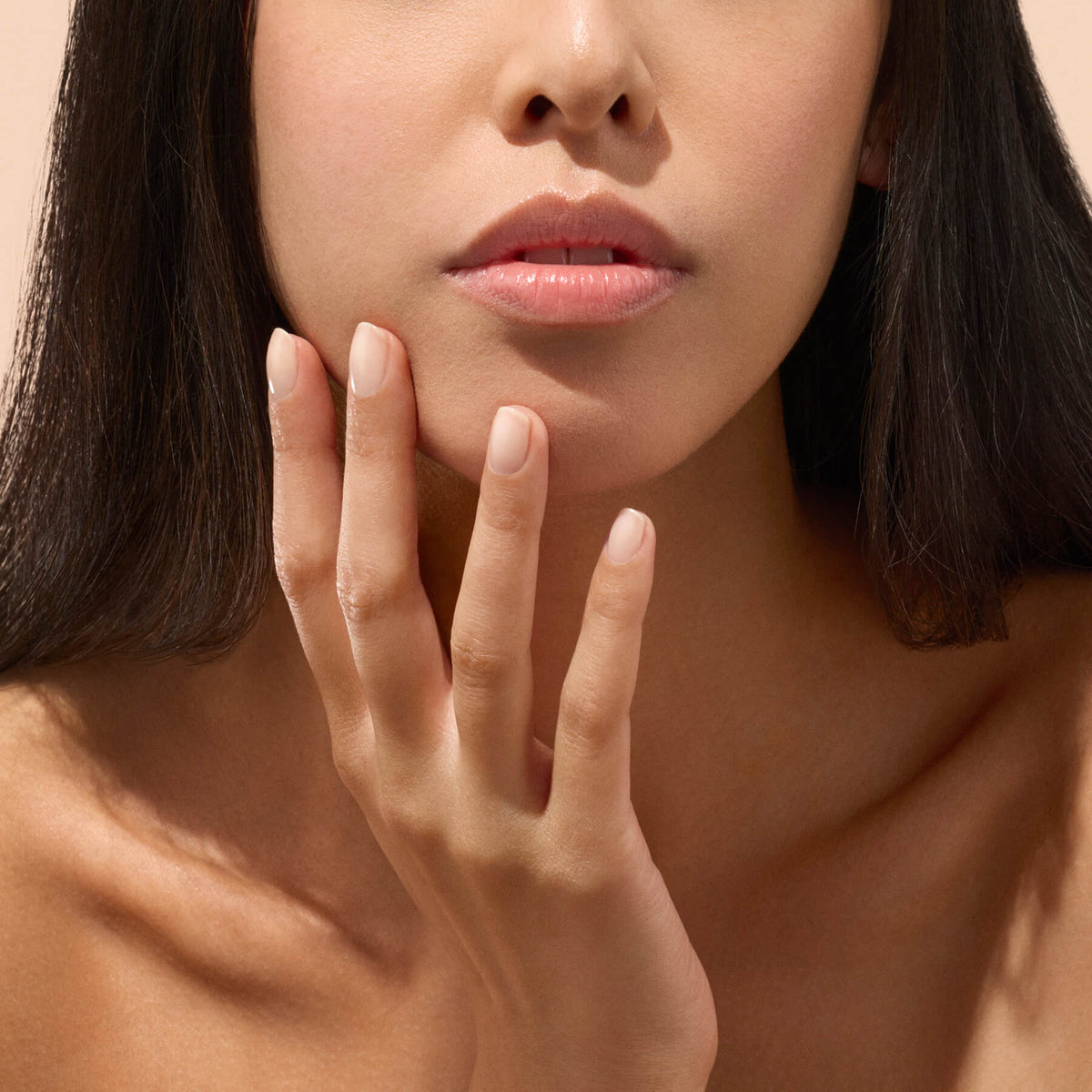 Une femme à la peau lisse touche doucement son visage de la main, mettant en valeur l’effet d’un soin des ongles minutieux. Ses lèvres sont légèrement entrouvertes et ses ongles paraissent sains et naturels — probablement grâce à Manucurist Active™ Smooth 01. Seuls le bas de son visage, son cou et sa clavicule sont visibles sur un fond neutre.