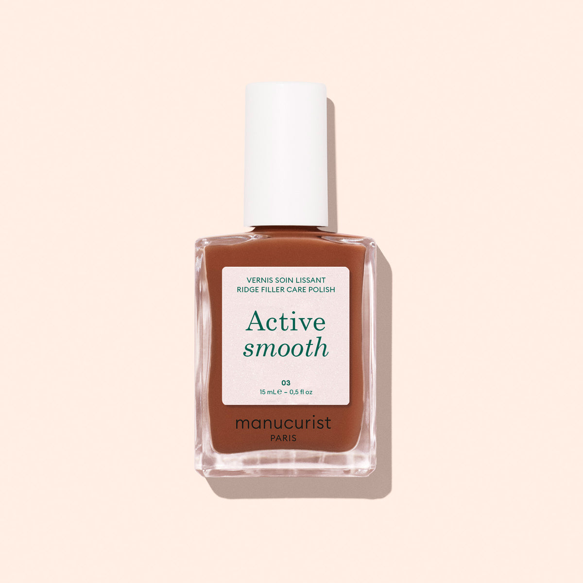 Un flacon de soin pour ongles Active Smooth 03 de Manucurist avec un bouchon blanc, un flacon en verre transparent et une étiquette beige-brun, présenté sur un fond rose pâle.