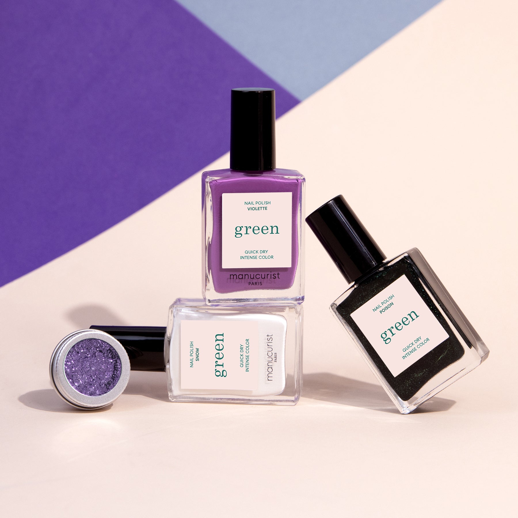 Three bottles of Manucurist’s Witchy Wicked nail polish in purple, black, and clear, plus a pot of shimmery purple powder—perfect for Halloween nail art—are displayed on a geometric pastel background.