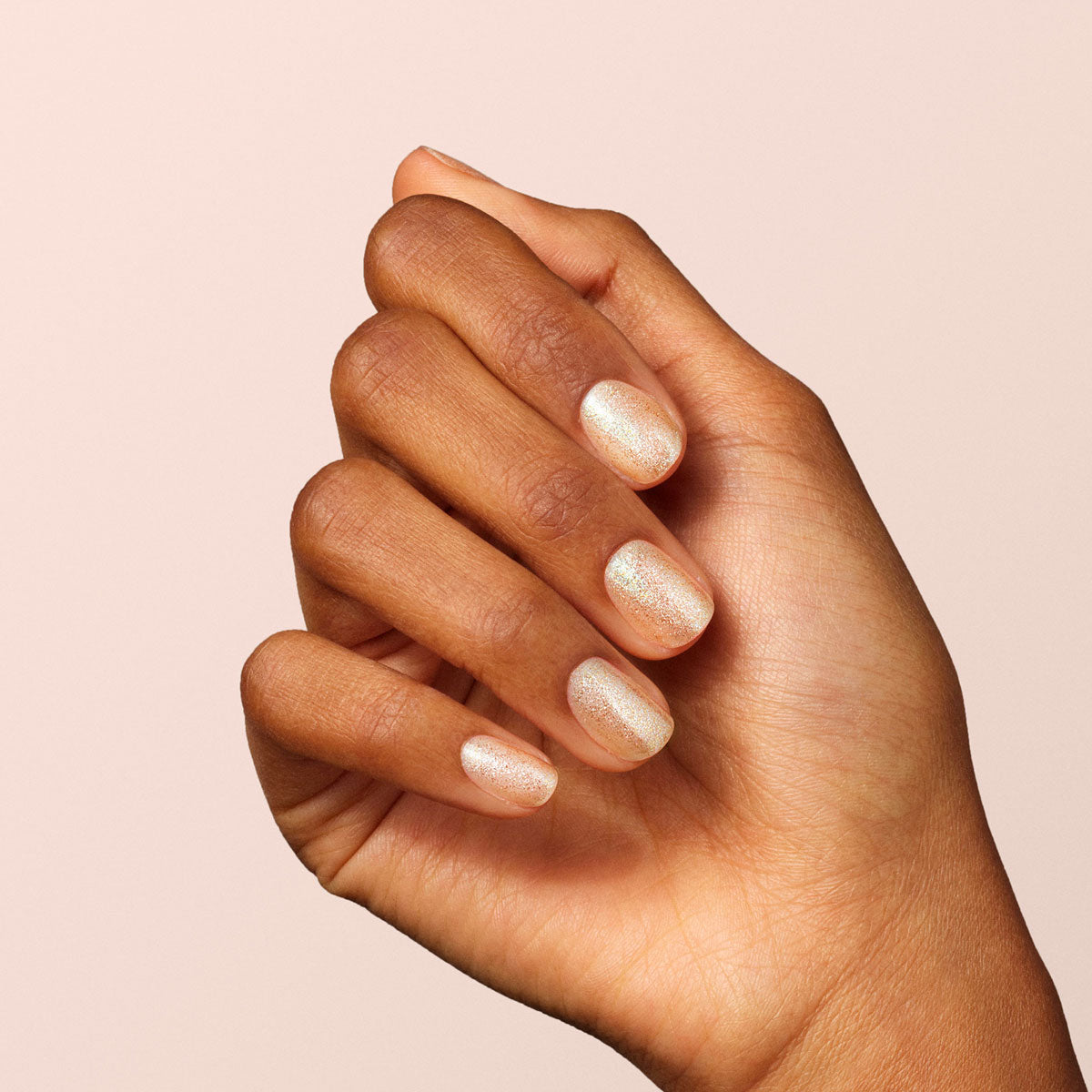 A hand with medium brown skin tone displays short, neatly manicured nails painted with Manucurist&