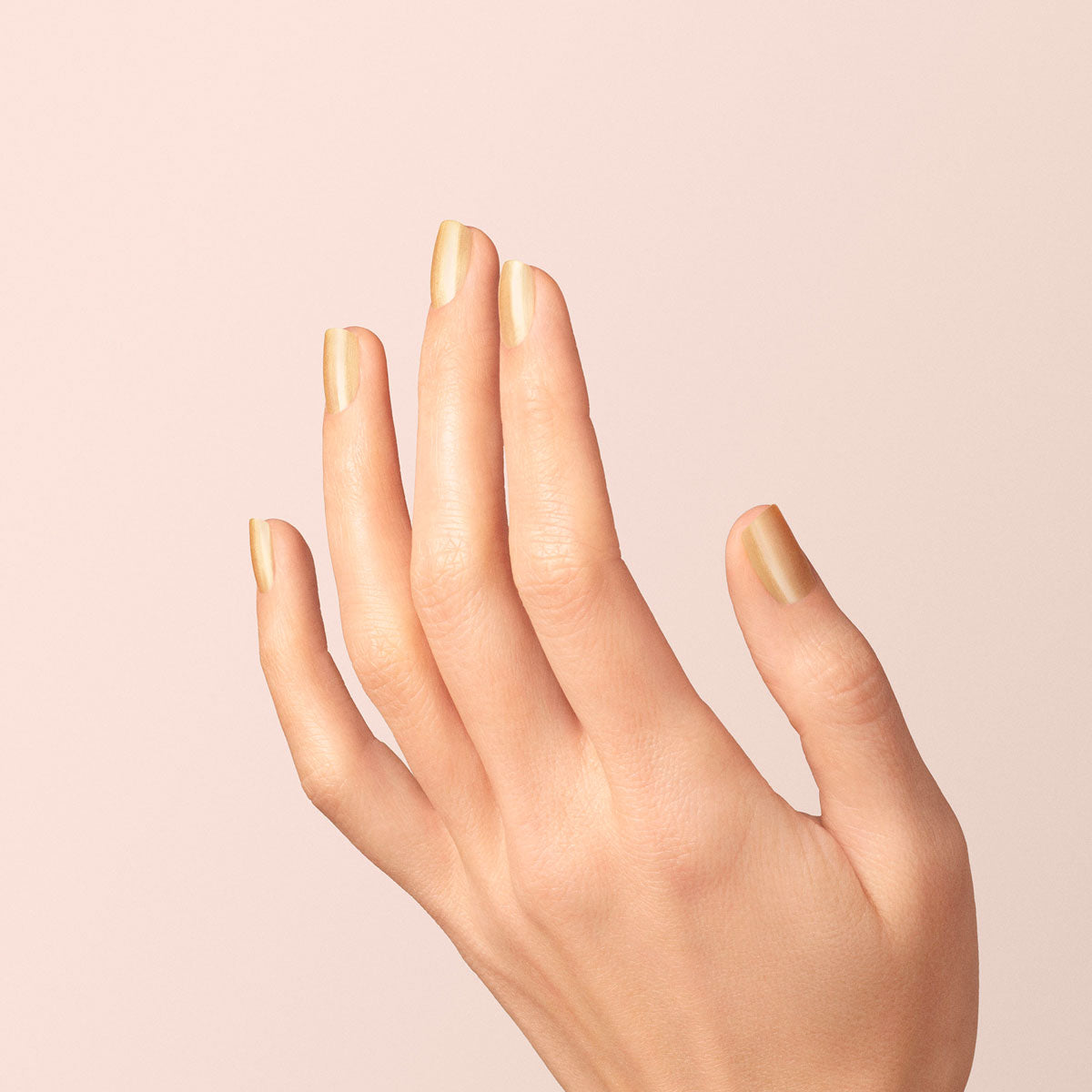 A hand with neatly manicured nails painted in Manucurist’s Gold Sand is held up against a soft, light beige background.