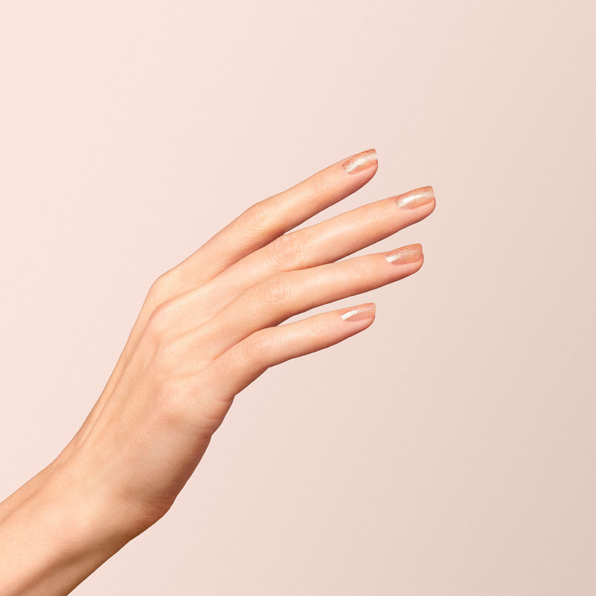 A hand with neatly manicured nails painted in a light nude shade features relaxed fingers and a hint of shimmer from Manucurist Gold nail polish, shown against a soft beige background.