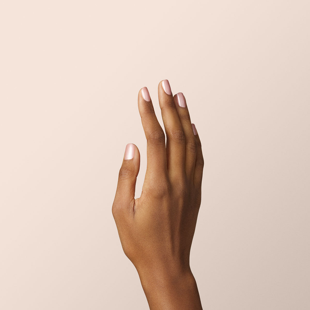 Une main à la peau brun moyen est tenue droite sur un fond beige clair, les doigts légèrement écartés et les ongles naturels soigneusement coupés — parfaitement préparée pour une manucure au vernis gel Green Flash Carnation de Manucurist.