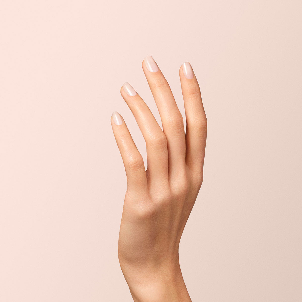 Gros plan sur une main aux doigts fins et aux ongles soigneusement manucurés, peints avec le vernis gel Milky White de Manucurist, sur un fond beige doux. La main est légèrement levée et délicatement courbée.