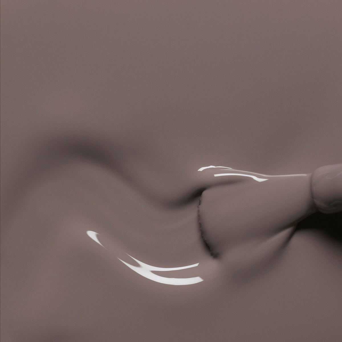 A close-up of a brush spreading glossy Clay nail polish from Manucurist, creating smooth, wavy patterns and shiny reflections on the liquid surface.