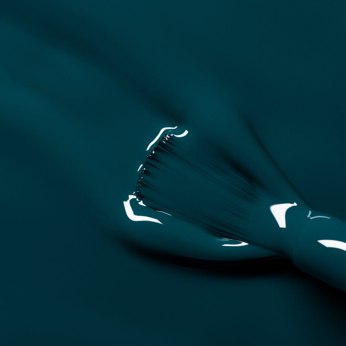 A close-up of a brush applying Manucurist’s Dark Clover nail polish, showing smooth, glossy teal strokes and reflective highlights on the freshly painted surface.