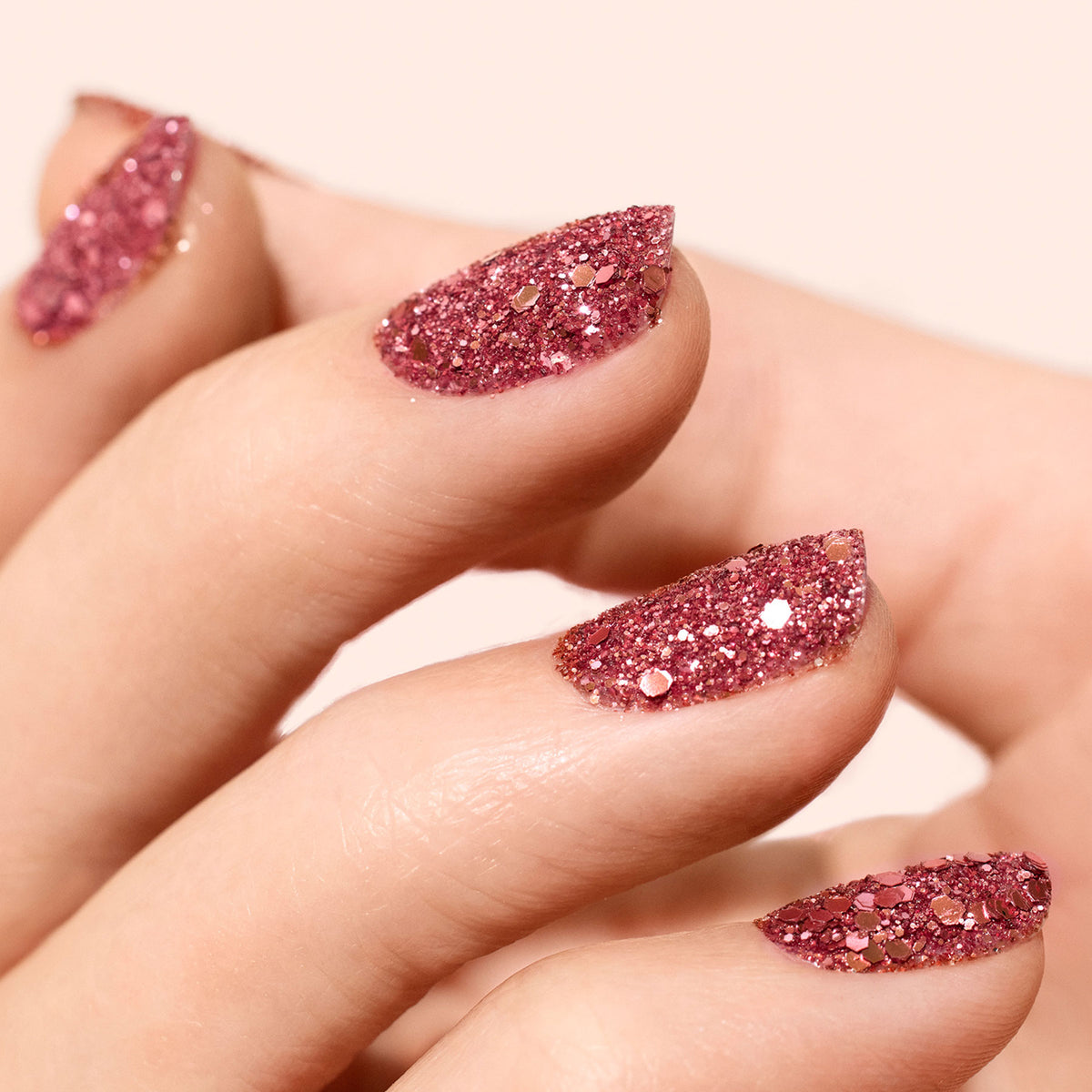 A close-up of almond-shaped nails painted with Manucurist Pink Quartz Biodegradable Glitter. The sparkly, glossy pink hues shimmer against a soft pale background.