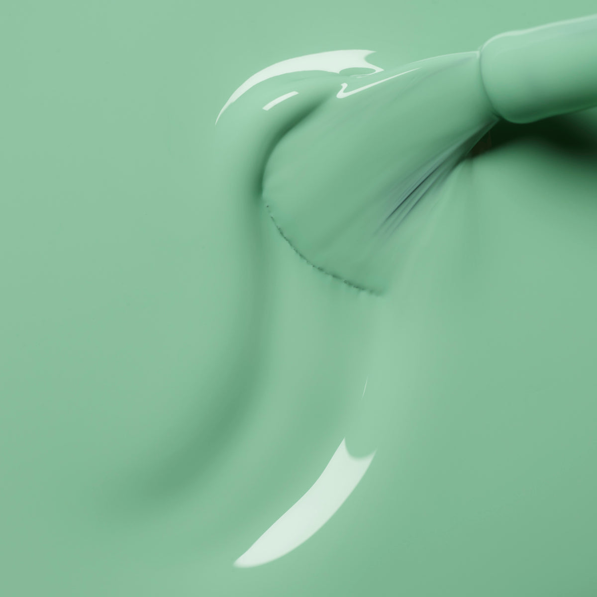 Gros plan sur un pinceau appliquant le vernis vert menthe brillant Amande de Manucurist en gestes fluides, mettant en lumière la texture visible et les reflets sur la surface humide.
