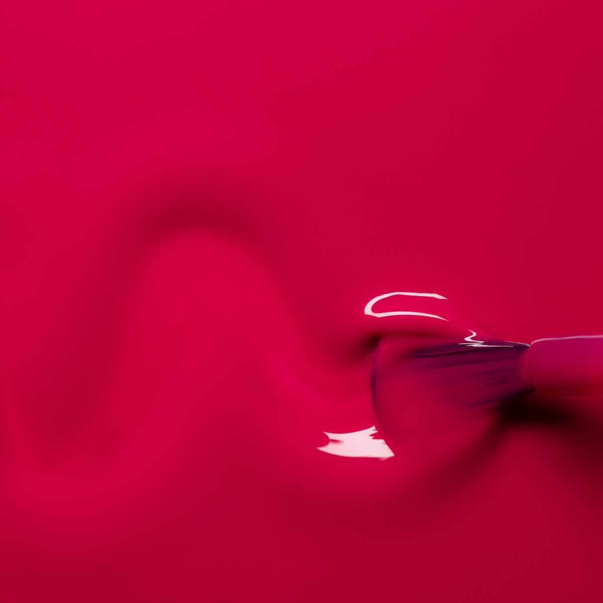 Gros plan d’un pinceau étalant le vernis gel Fuchsia de Manucurist en ligne ondulée sur une surface lisse, avec des reflets brillants mettant en valeur la couleur rose vibrante.